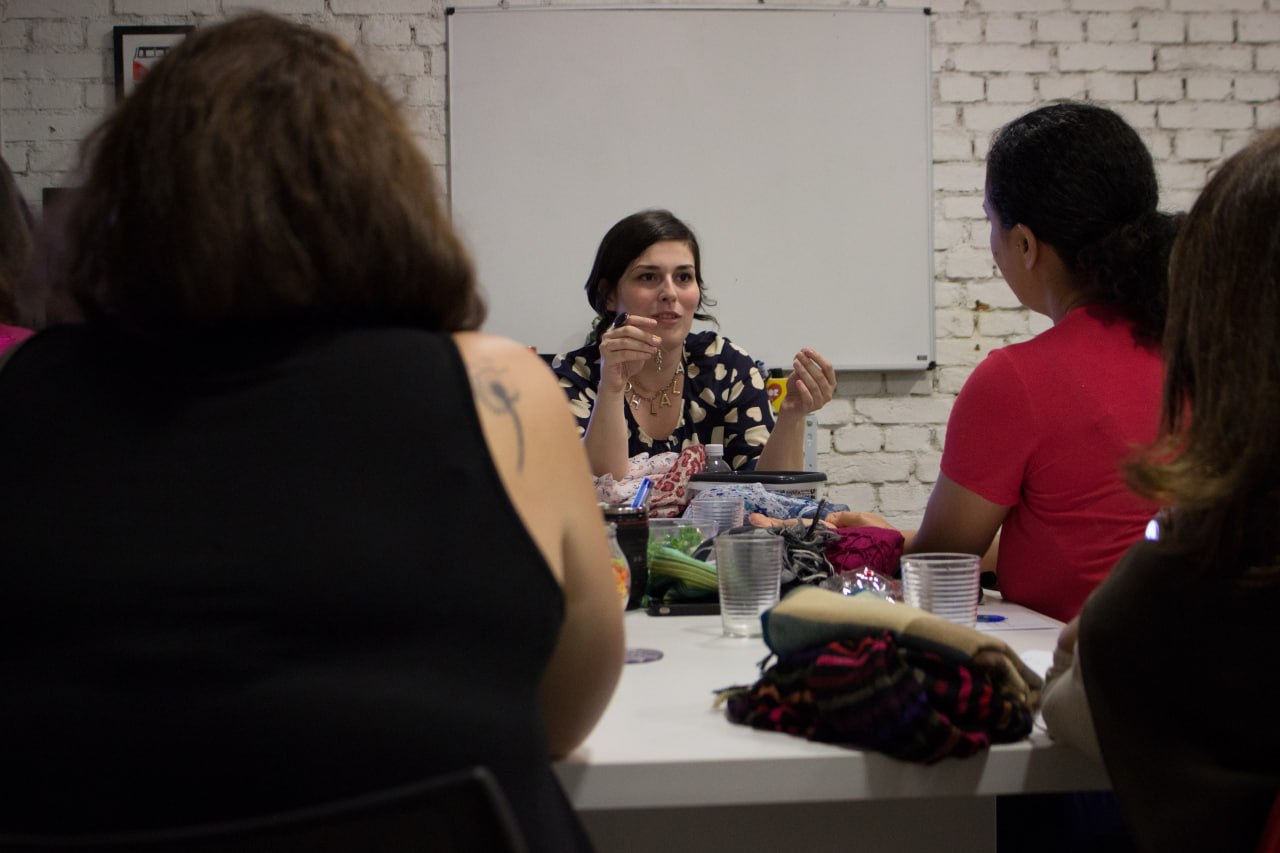 Érica Minchin conduzindo um encontro com um grupo de consultoras sentadas em volta de uma mesa.